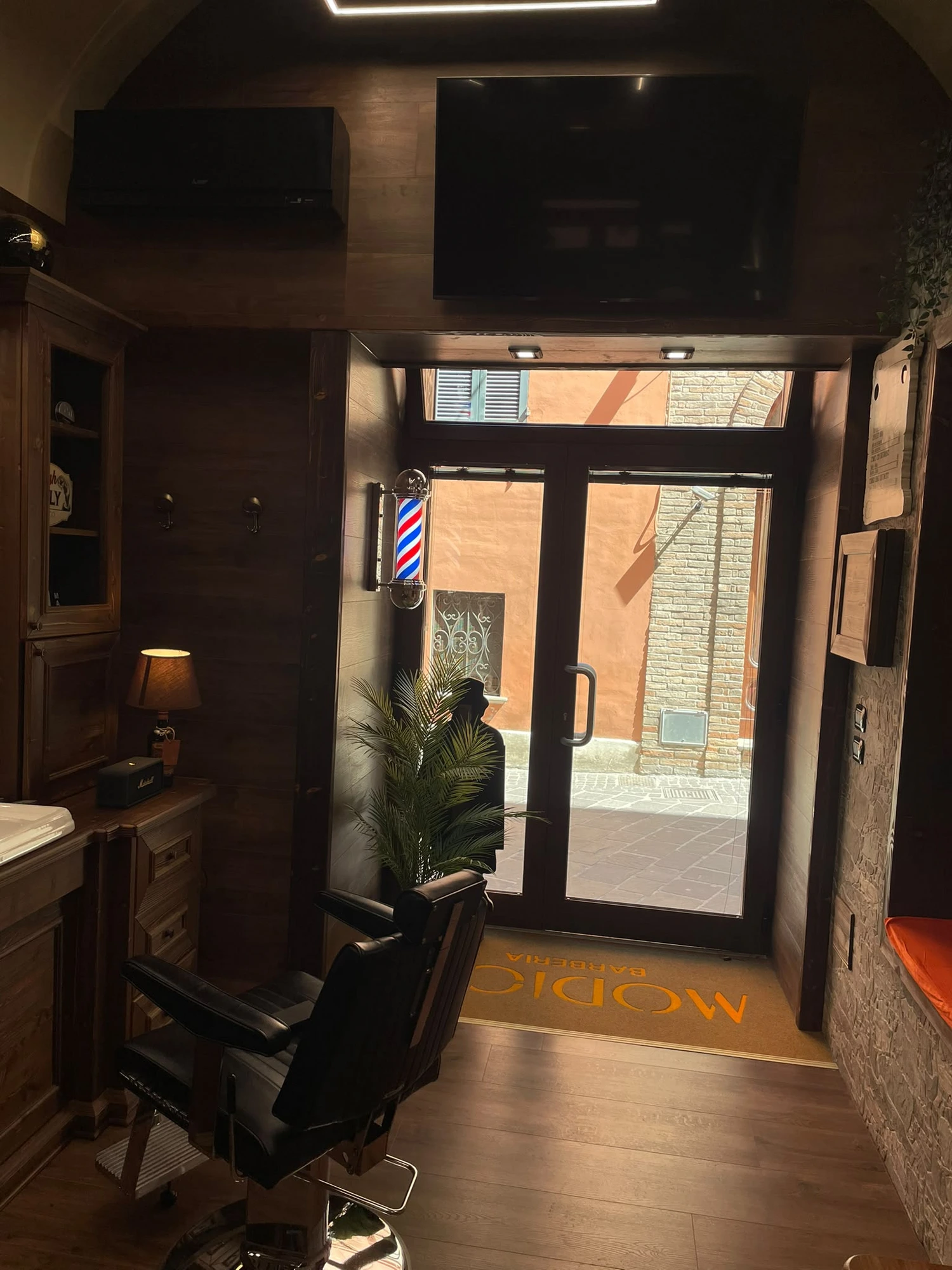 Sala principale di Modico Barberia con logo MB arancione e poltrone in pelle nera