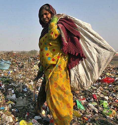 A waste picker walking through an Indian landfill carrying a sack of collected plastic