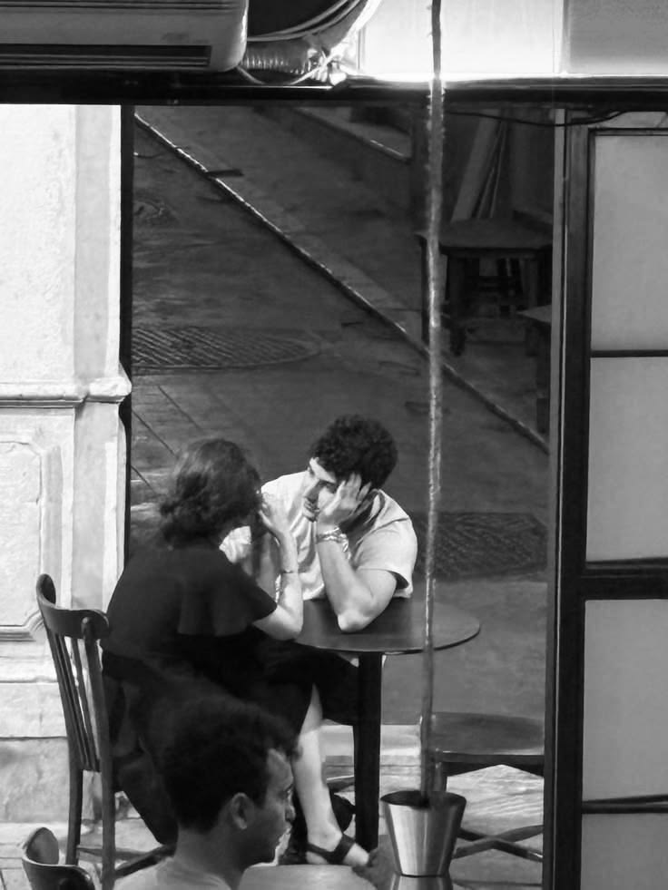 A black-and-white film photograph of a couple deep in conversation at a café